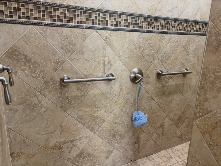 Two stainless grab bars installed on a tiled shower wall