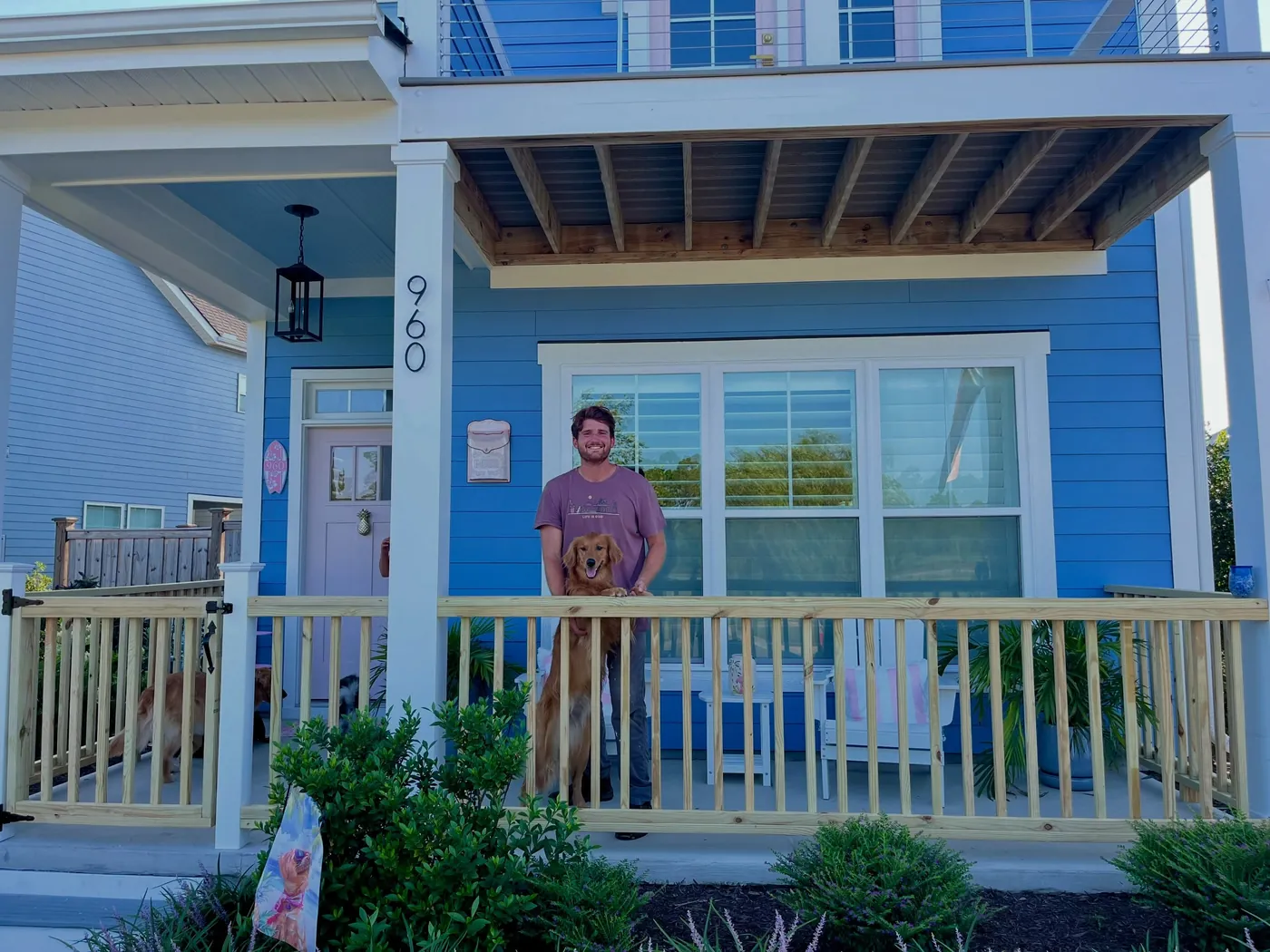 Owen standing on a front porch he fenced in with white pickets, in front of a blue house